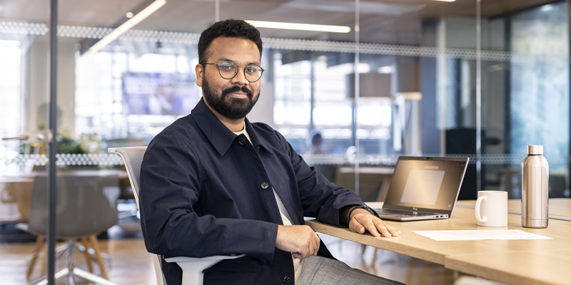 A mature student sat at a desk using a laptop in a bright, modern office space.