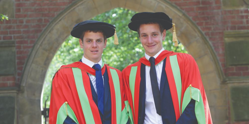 Two honorary graduates stand for photos beneath an archway at the University of Leeds