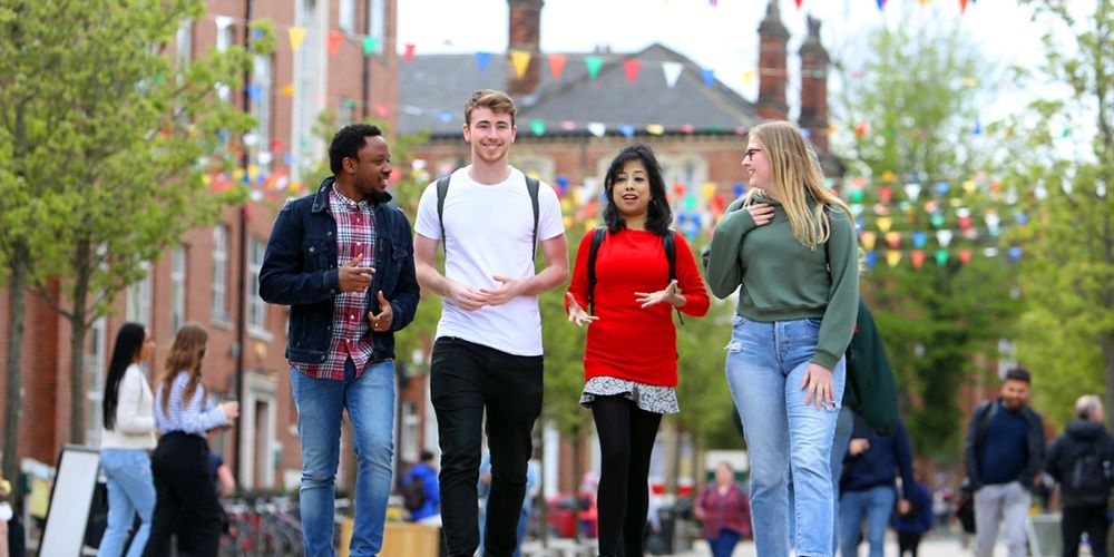 A group of four postgraduates walking outside on campus, past the Student Union, chatting and smiling.