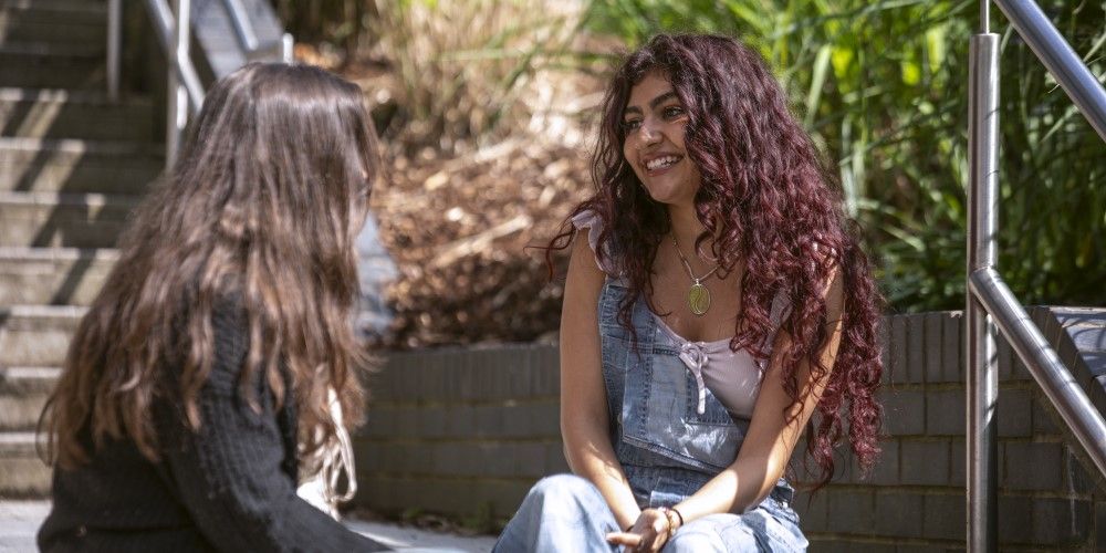 Two students sitting on steps on campus, smiling and talking together.