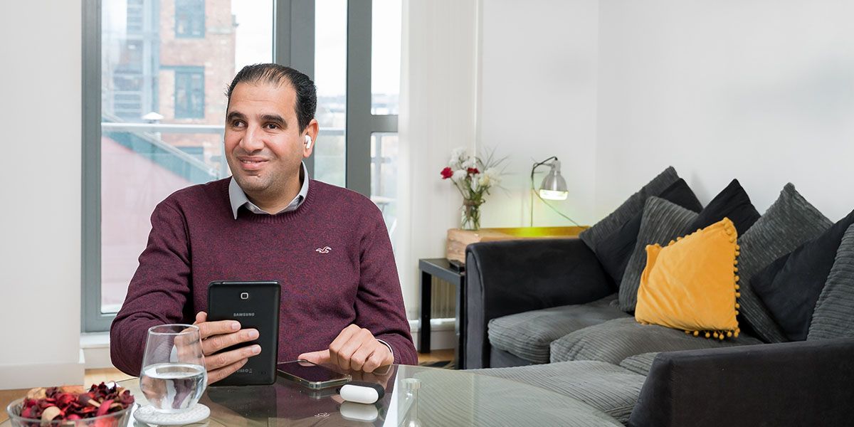 A man sat at a table using a tablet with ear buds.