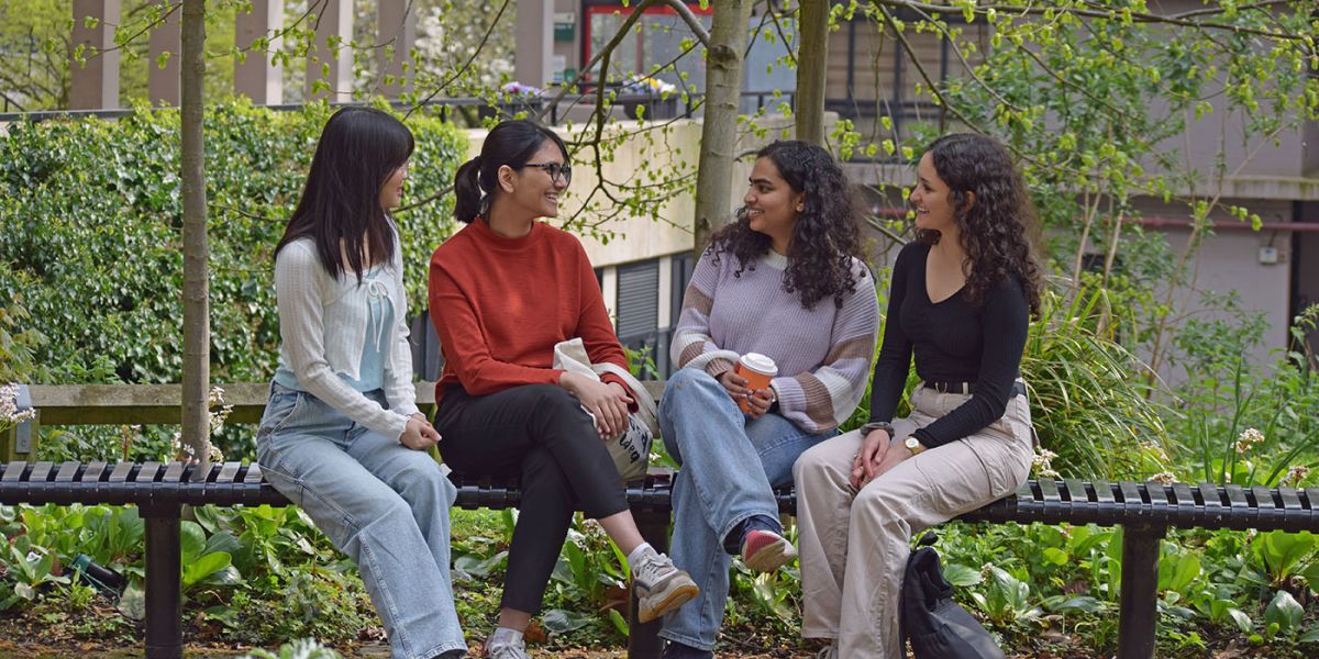 Four students sat on a bench smiling.