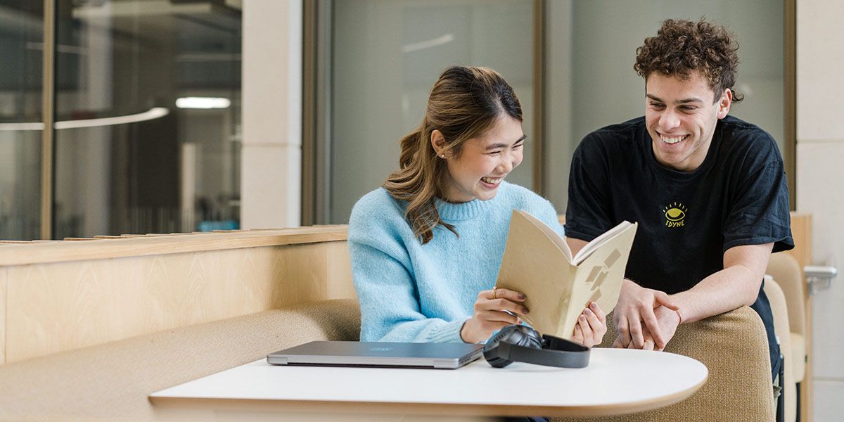 Two students smiling in a study space, using a laptop.