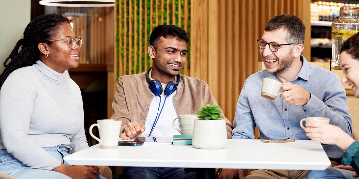 Front close view of four students sitting around a table, enjoying a coffee in a cafe on campus.