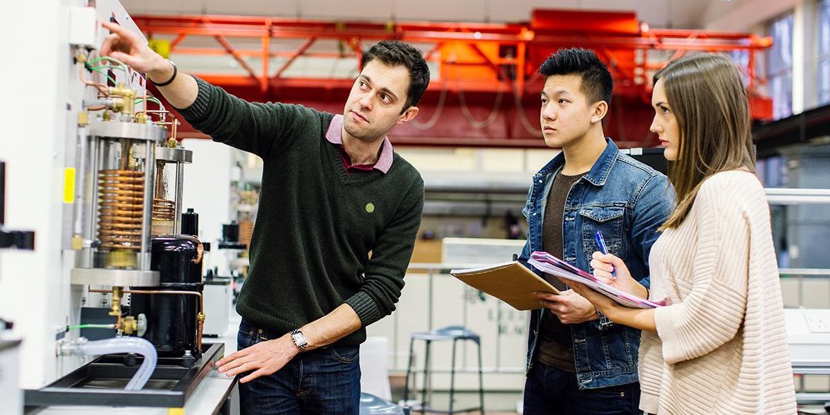 两名机械工程专业的学生在实验室做笔记，作为讲师指着一台机器