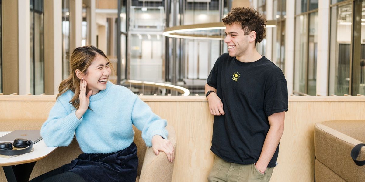 Two students in a modern and bright space with sofas on campus, chatting and smiling.