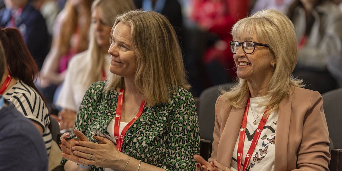Two teachers sat smiling at a conference.