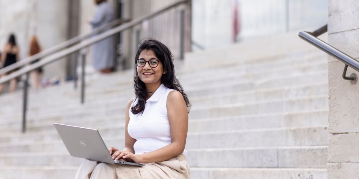 A student sat on the Parkinson steps, with an open laptop on their knee.