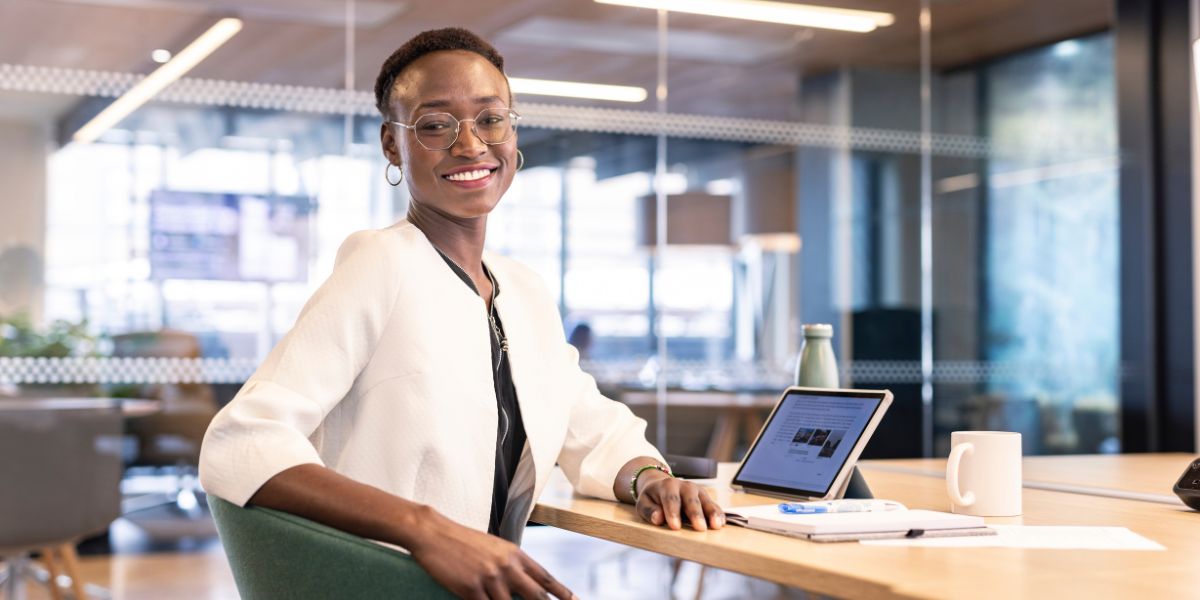 A student sat at a table working on a laptop. They are smiling.