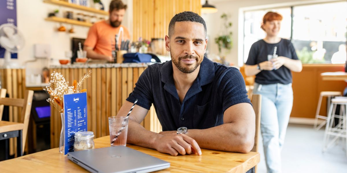 An online student sat in a cafe, with their laptop on their table.