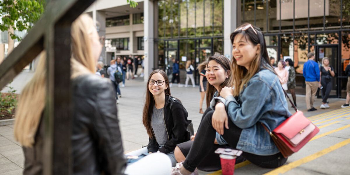 Students sat on an outdoor staircase on campus, smiling and chatting