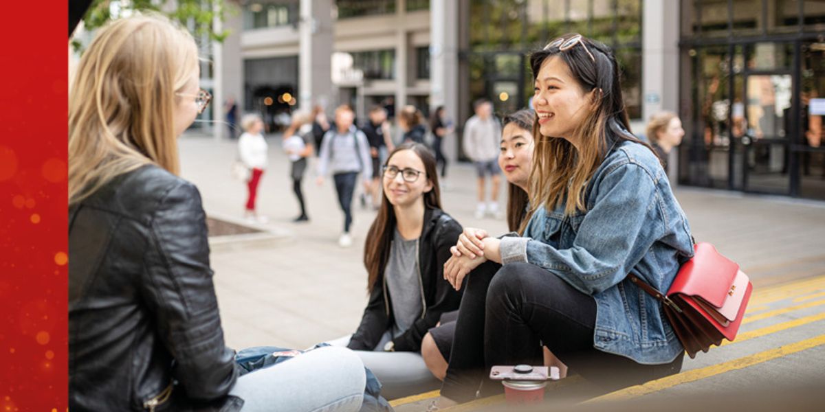 Students sat on an outdoor staircase on campus, smiling and chatting