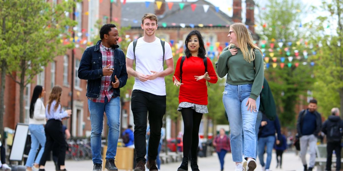 A group of four postgraduates walking outside on campus, past the Student Union, chatting and smiling.