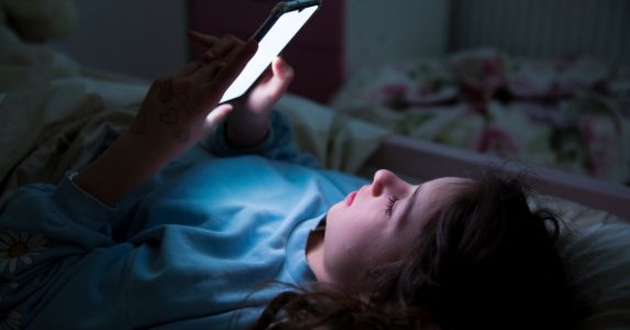 A child using a smartphone late at night lying in bed.