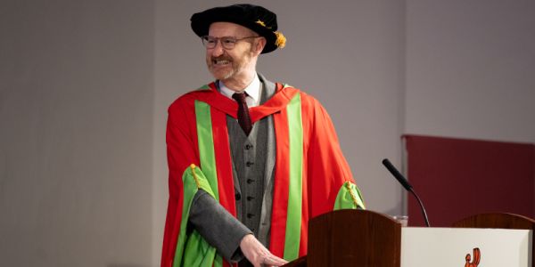 Graduate stands at lectern in academic attire, smiling