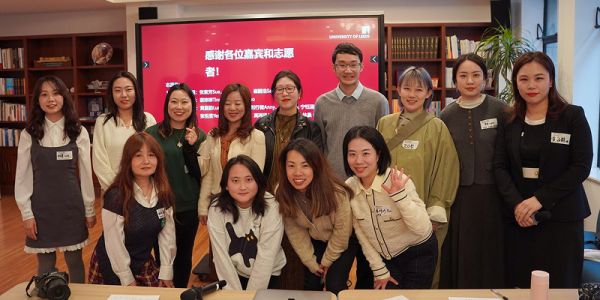 A group of alumni pose for a picture in front of a display screen at an event