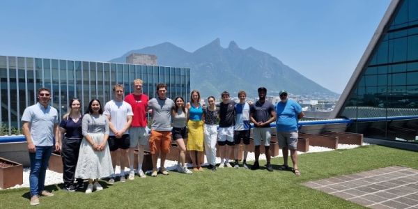 A large group of students stood on a rooftop with a building and a mountain in the background.