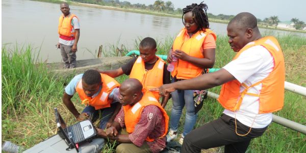 In the foreground, researchers in orange high vis-vests conducting field measurements on the Kasai River, one of the major tributaries of the Congo basin