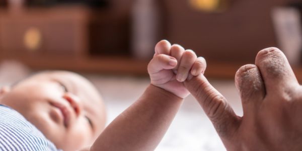 A baby grasps their parent's little finger.