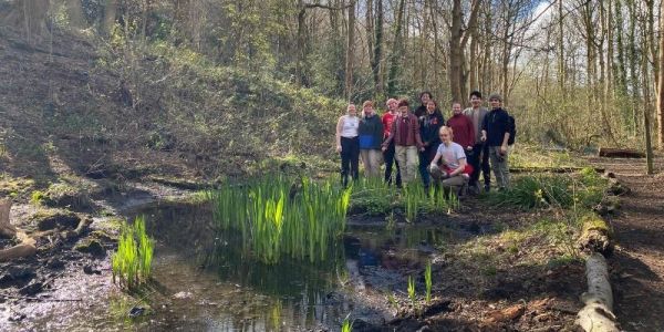 A group of students stand by the wetland area they help manage in Woodhouse Ridge.