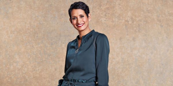 Naga Munchetty, wearing a grey dress, smiles at the camera in front of a beige background