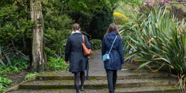 Two women walk up some steps into a tree-lined path in a park