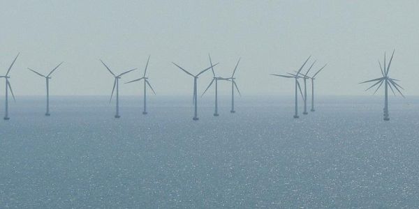 The images shows an offshore windfarm on a calm  day. The sea is flat.
