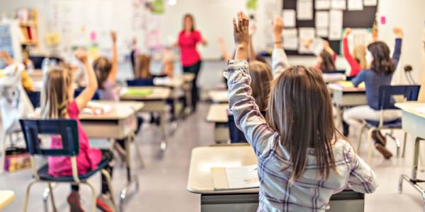 Children seated in a classroom raising their hands