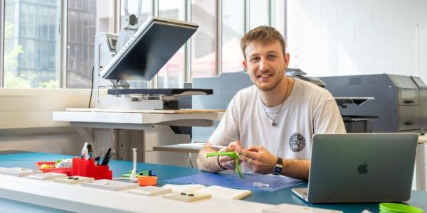 Tom Milner is sat at a desk in Helix on the University of Leeds campus making one of his bracketless plant pot holders.