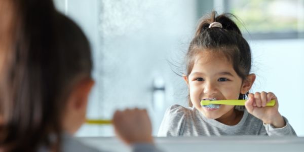 A child brushes their teeth in the mirror.