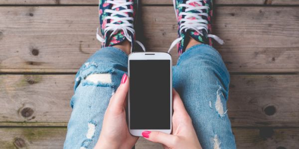 An image of a young person's knees as she looks down at a mobile phone in their hands