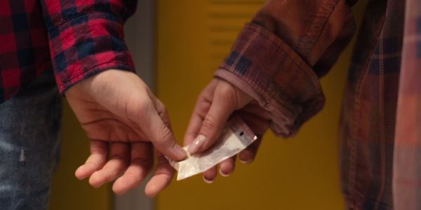 A student's hand passing a bag of white powder into another student's hand