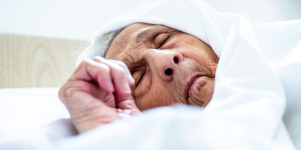 An elderly person wearing a headscarf, ill in bed