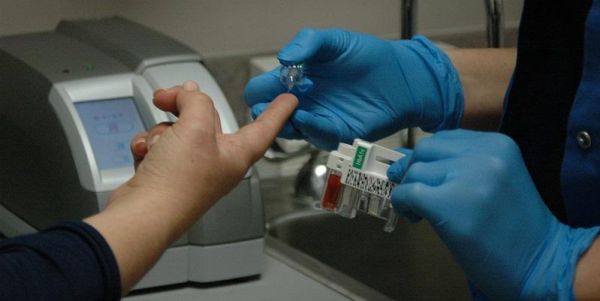The image shows a patient having a finger-prick blood test for diabetes.