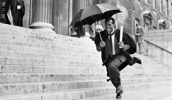 Alum Cec Thompson running on the Parkinson steps holding an umbrella and a scroll.