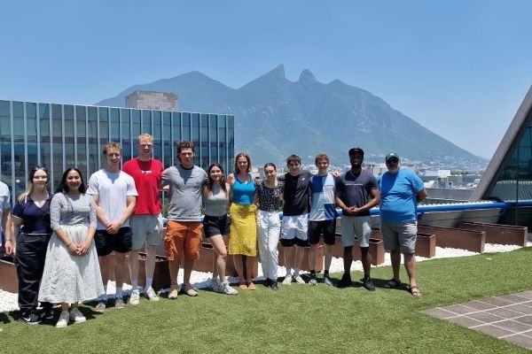 A large group of students stood on a rooftop with a building and a mountain in the background.