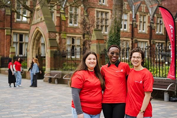 Three smiling student ambassadors in red t-shirts stand together outside Clothworkers Court.