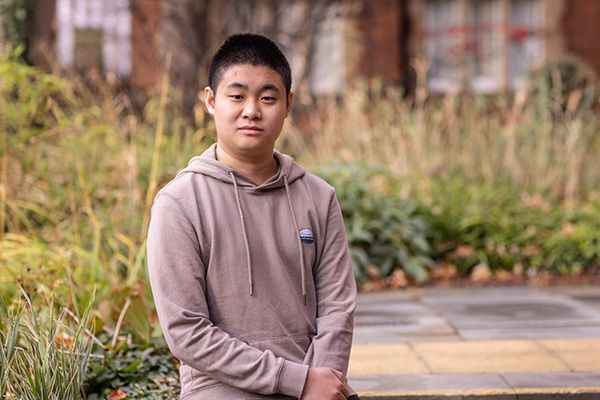 Portrait of Andy Zhang, sat smiling in a garden on campus.