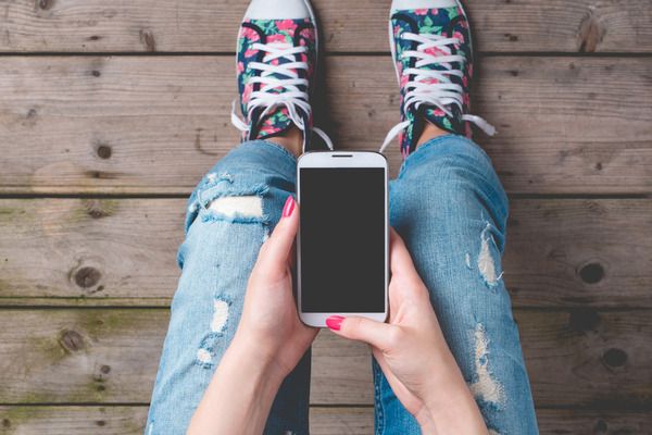 An image of a young woman's knees as she looks down at a mobile phone in her hands