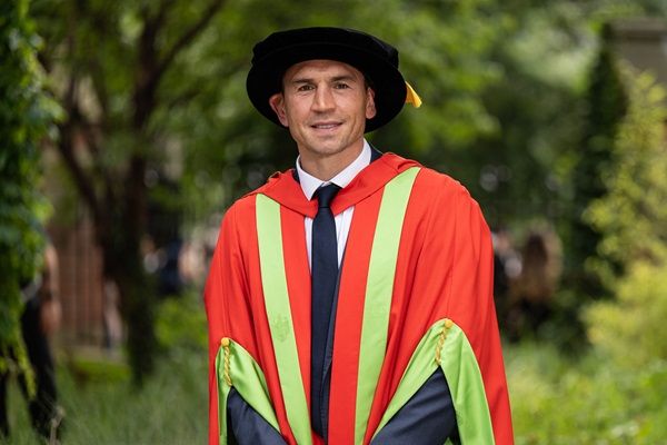 Kevin Sinfield stood outside on campus on a sunny day wearing graduation cap and gown.