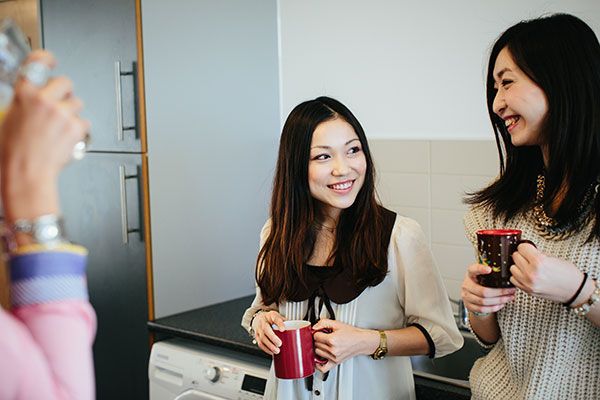 两名女生站起来，在大学宿舍厨房大厅里聊天。