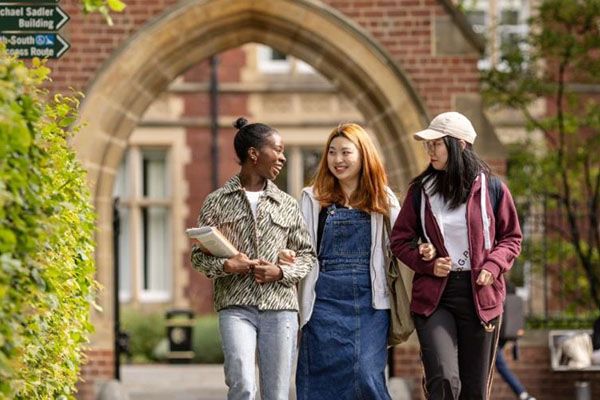 Three students smiling as they walk beneath the arch of Clothworkers' court.