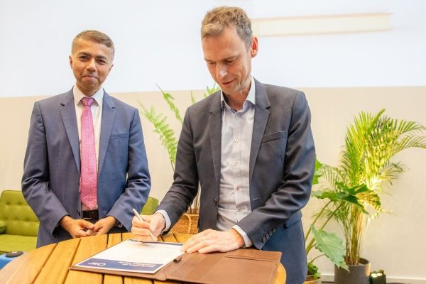 Masud Khokhar and Jeroen Geurts both wearing suits signing a document.