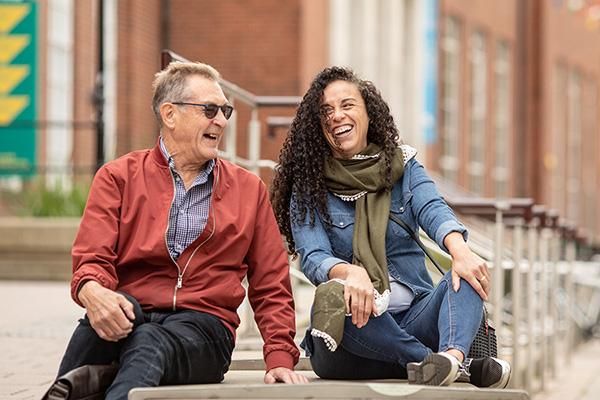 Two mature students sitting and laughing outside Leeds University Union