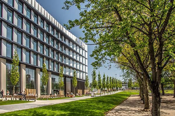 the exterior of the Nexus building and a tree lined street with people sitting on picnic benches