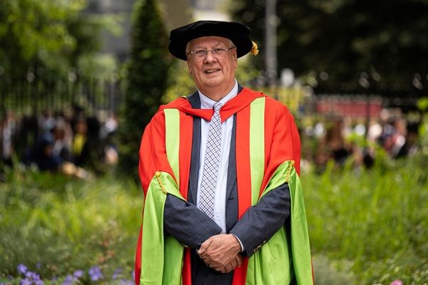 Peter Buckley stood on campus on a sunny day wearing graduation cap and gown.