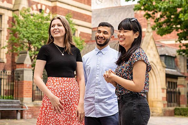 Three postgraduate students on campus outside The Great Hall.