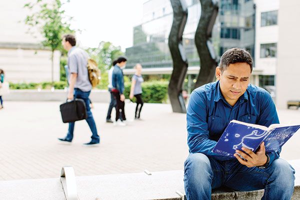 一名硕士生坐在艺术雕塑招牌附近的山毛榉林广场读书。