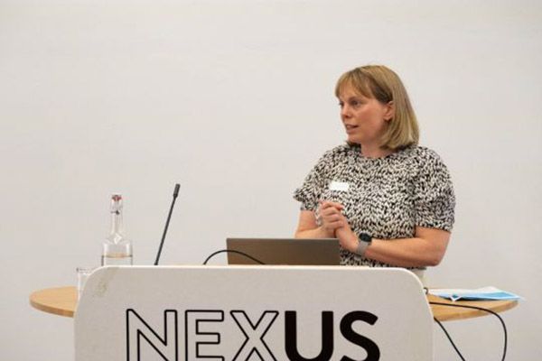 Sarah Astill presenting in front of a podium that says NEXUS.