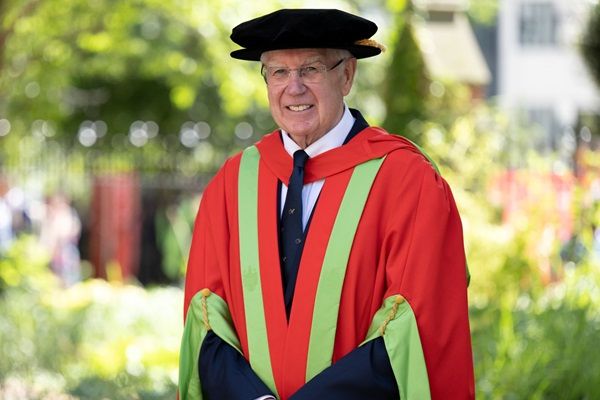 Alan Langlands stood outside on campus on a sunny day wearing graduation cap and gown.